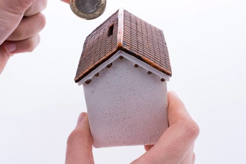 Hand dropping coin into the moneybox in the shape of a model house
