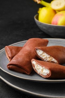 Closeup view of thin chocolate pancakes stuffed with curd