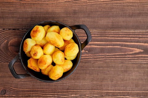 Top view of baked potato in cast iron skillet on natural wooden background