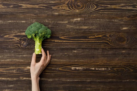 Overhead view of fresh broccoli in hands over wooden background