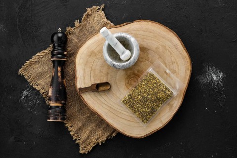 Wooden cross section with lemon pepper in plastic package and stone mortar and mill
