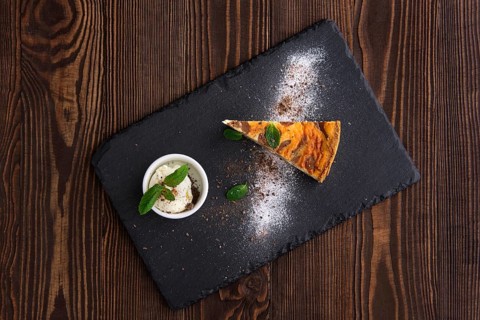 Top view of layered cheesecake with ice cream served on slate plate on dark wooden background