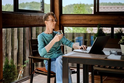 Middle aged man drinking wine and chatting in messenger on laptop