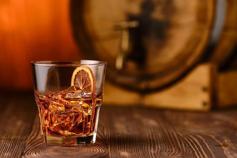 Glass of cocktail with whisky and orange liquor with barrel on background