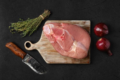 Overhead view of raw slice of beef steamship round with cooking ingredients on black background