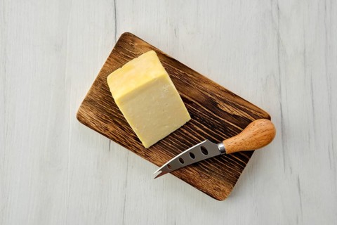 Top view of triangular piece of hard cheese on wooden cutting board