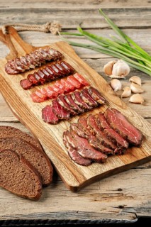 Slices of smoked dried beef and pork meat on wooden cutting board