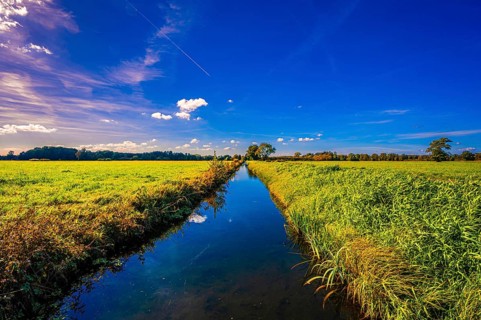 A small irrigation canal between two fields with reflection of clouds and the blue sky in autumn
