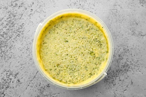 Top view of homemade soft cheese with herbs in plastic bowl