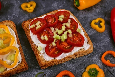 Slice of healthy whole grain toast topped with vegetables like red cherry tomatoes and cucumber pieces