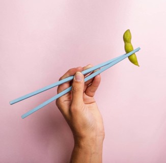Hand holding chopsticks with edamame bean