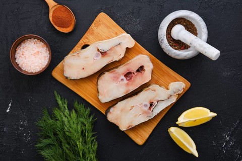 Top view of fresh raw cod steak on wooden cutting board with spice