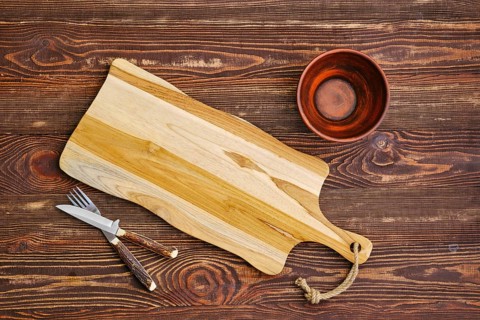 Top view of empty cutting wooden board with clay bowl and fork with knife on the table