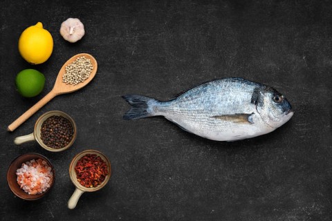 Overhead view of fresh raw gilt head bream with spice on black stone background