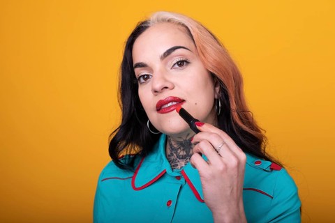 Beautiful caucasian woman applying a bright red color lipstick on her lips over yellow background