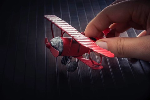 Hand holding a red toy plane on a on wooden texture