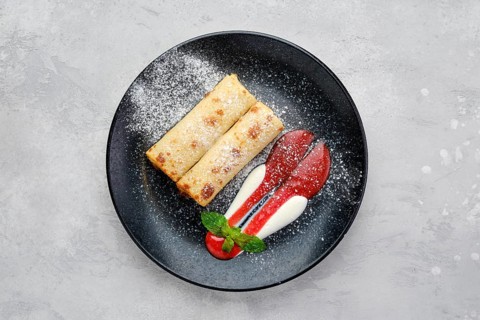 Top view of thin crepe stuffed with cottage cheese served with strawberry jam and sour cream