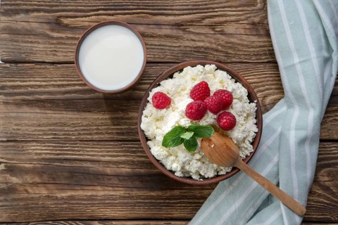 Fresh cottage cheese with raspberries and wooden spoon in clayware on wooden table