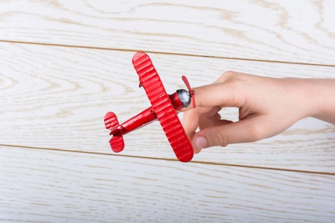 Hand holding a red toy plane on a on wooden texture