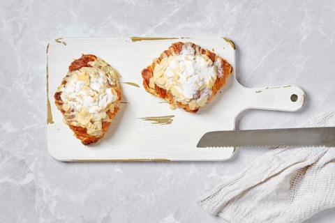 Top view of crispy croissant with caramel and peanut shavings on white serving board on marble background