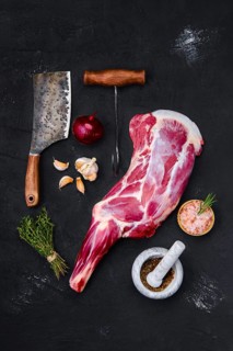 Fresh raw lamb leg bone in on wooden cutting board with herbs and seasoning