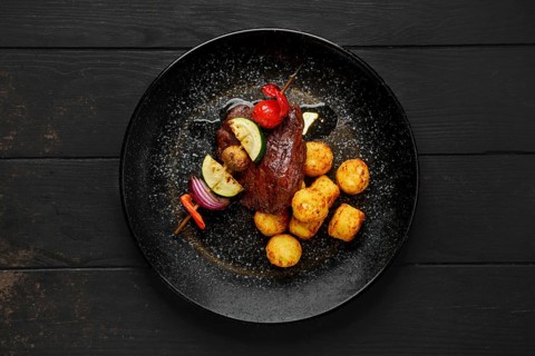 Top view of grilled beef with vegetables and potato balls on a plate
