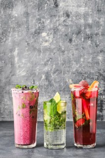 Three glasses with fruit refreshing drink on gray shabby background