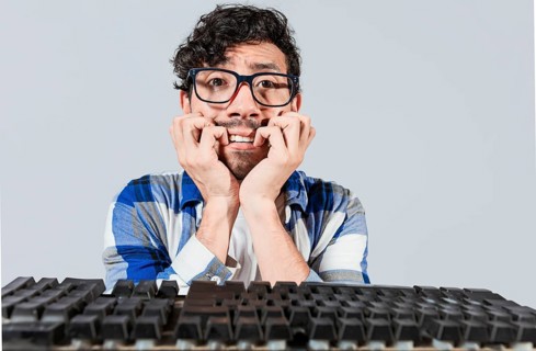 Nervous nerdy guy biting his nails in front of the keyboard