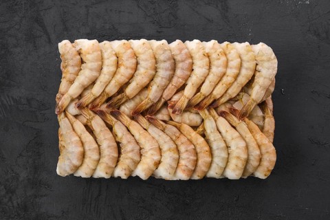 Overhead view of raw tiger shrimp frozen in large ice cube on black concrete background