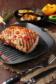 Grilled striploin on cast iron skillet and fried eggplant on wooden background