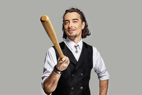 Dramatic man in white shirt and black vest with long curly hair holding baseball bat