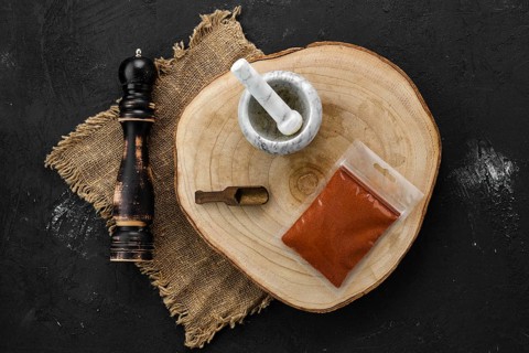Wooden cross section with chilli pepper in plastic package and stone mortar and mill