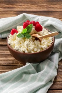 Fresh cottage cheese with raspberries and wooden spoon in clayware on wooden table