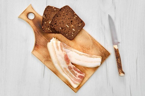 Top view of two slices of bacon and brown bread on wooden cutting board