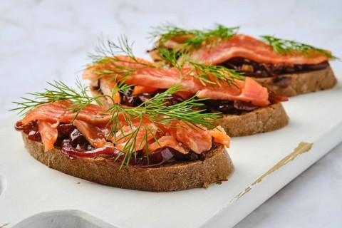 Closeup view of salmon sandwich with caramelized onion on wooden serving board