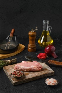 Raw veal steak bone in with ingredients for cooking on black background