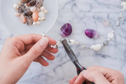 Close up woman s hand fixing bracelet with plier marble desk