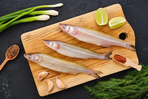 Top view of raw fresh smelt fish on wooden cutting board with spice and herbs