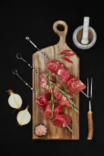 Top view of skewers with raw beef meat and spice on dark background