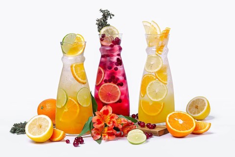 Three pitchers with summer fruit and berry cocktails on white background