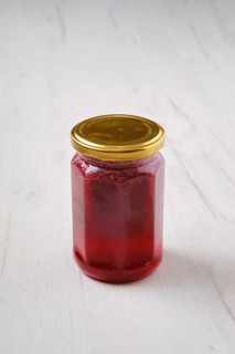 Whole closed jar of cherry jam on white wooden background