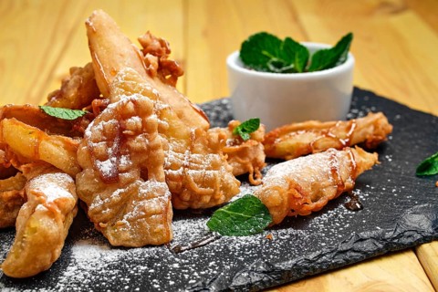 Close up view of deep fried fruits in breading served with caramel and strawberry jam