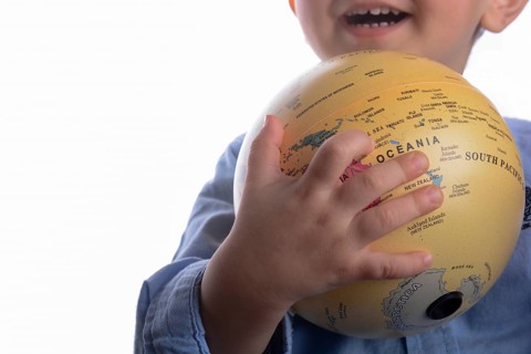 Baby with blue shirt holding a globe in hand on white background