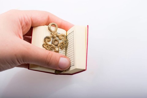 Hand holding Key and Islamic Holy Book Quran in mini size