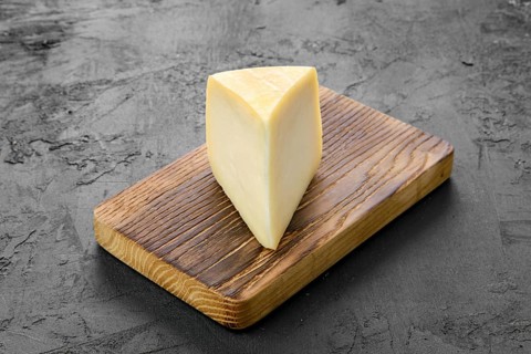 Triangular piece of goat cheese on wooden cutting board on black background