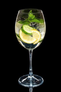 Cold Lemon and cucumber cocktail with a sparkling wine with ice cubes in wine glass isolated on black