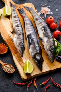 Raw fresh icefish on wooden cutting board with spice and herbs