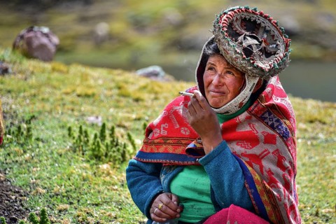 Quechua Indian woman in traditional dress sitting in a meadow smoking at Pacha Mama ceremony