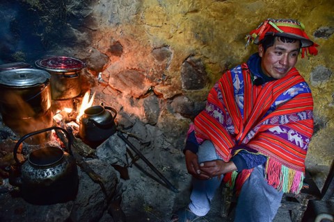 Quechua Indian in traditional dress cooking at the fireplace of his hut