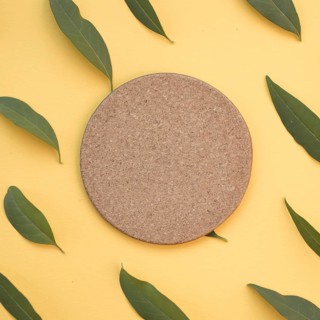 Blank circular cork surrounded with green leaves yellow background